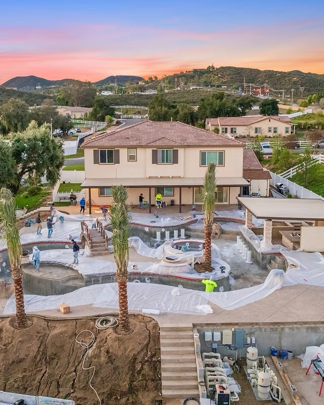Aerial view at sunset of a large custom pool and spa under construction with the Prime Time crew preparing the surfaces