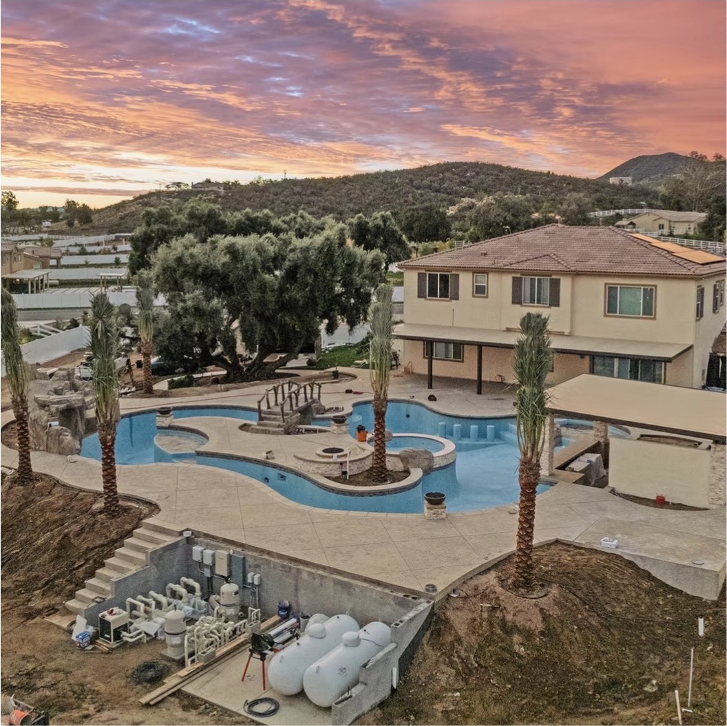 Finished lagoon pool, spa and swim-up bar at sunset with palm trees and hillside views