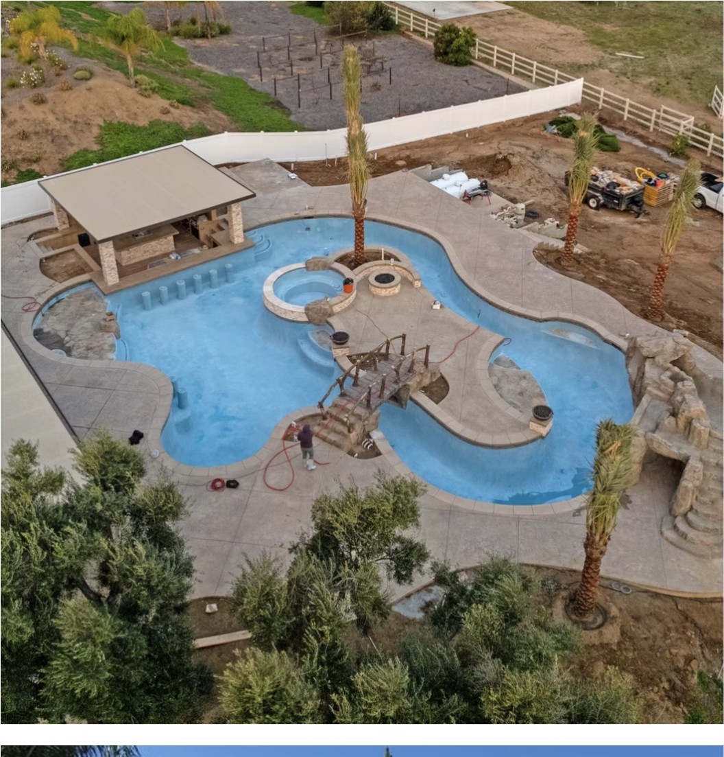 Aerial view of a completed freeform lagoon pool with spa, bridge, rock features and stamped concrete decking