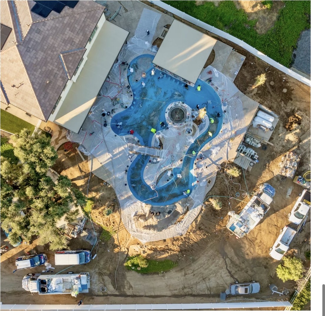 Overhead aerial of a curved lagoon pool and lazy river filling with fresh blue plaster